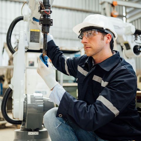 A man wearing a hard hat and goggles is working on a machine