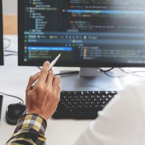 A person is holding a pen in front of a computer monitor