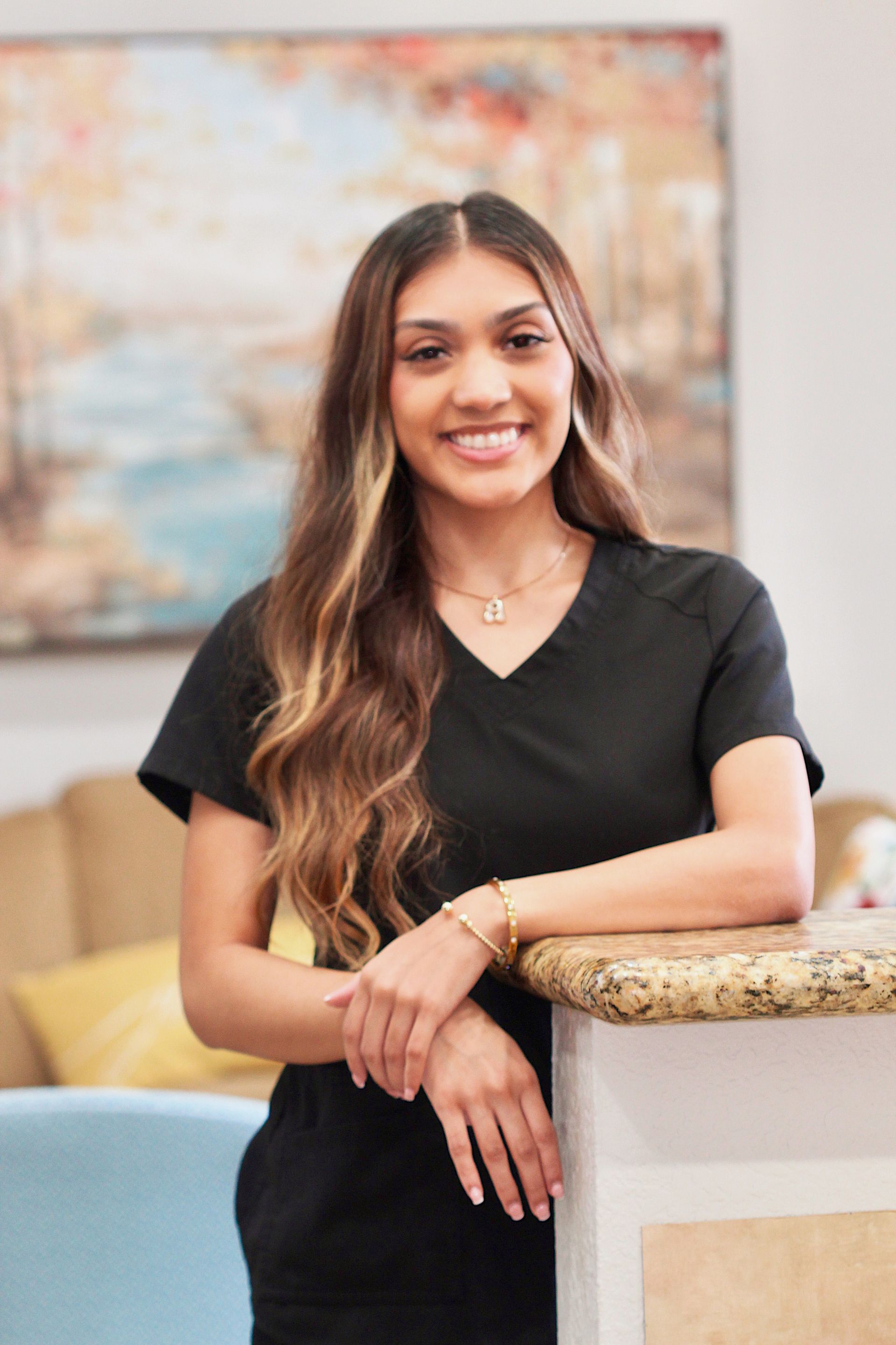 Smiling woman in black top leaning on a counter in a bright room with abstract wall art.