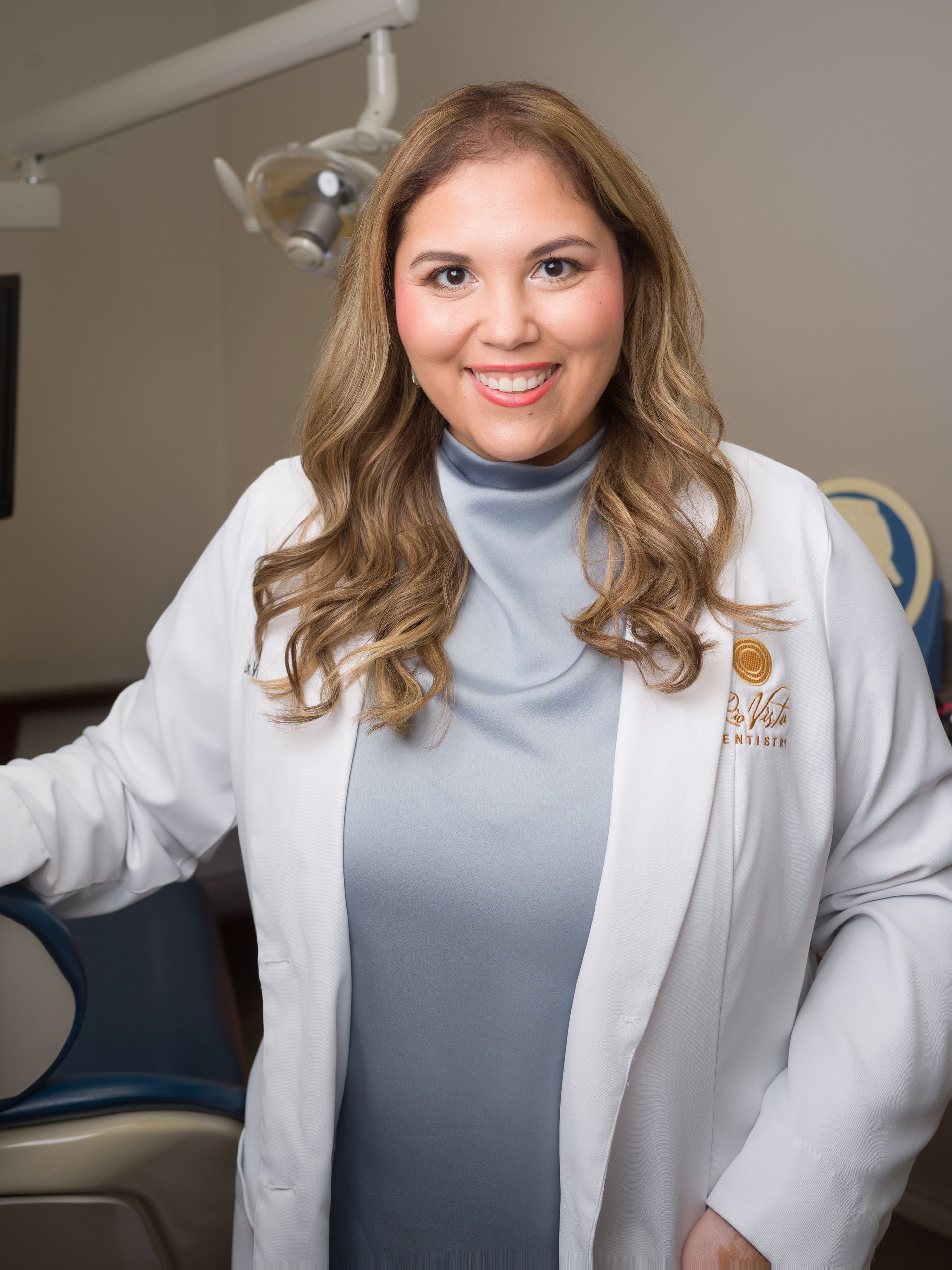 Woman in a white coat smiling in a medical exam room.
