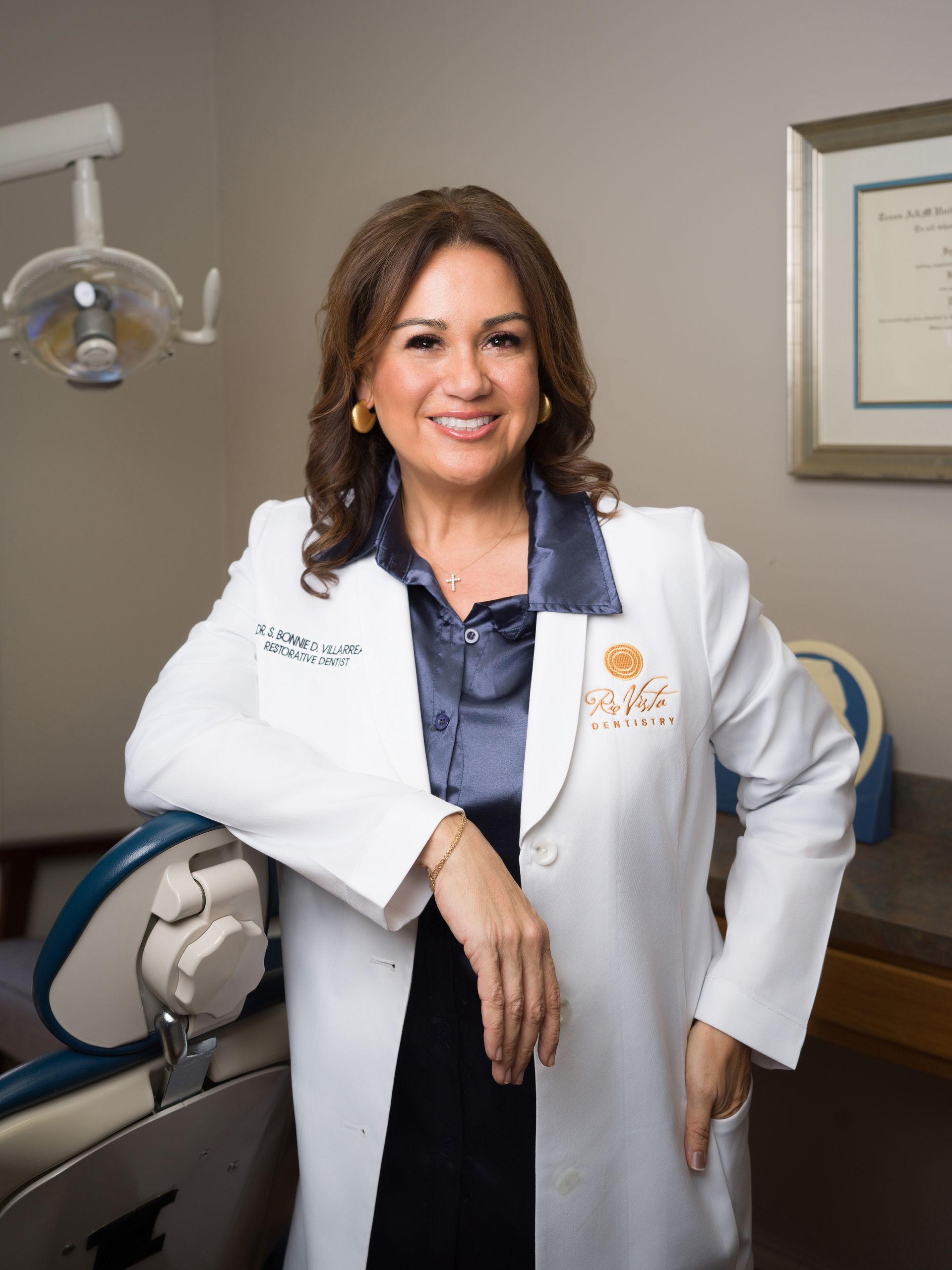 Smiling doctor in a white coat standing in a medical office beside an exam chair