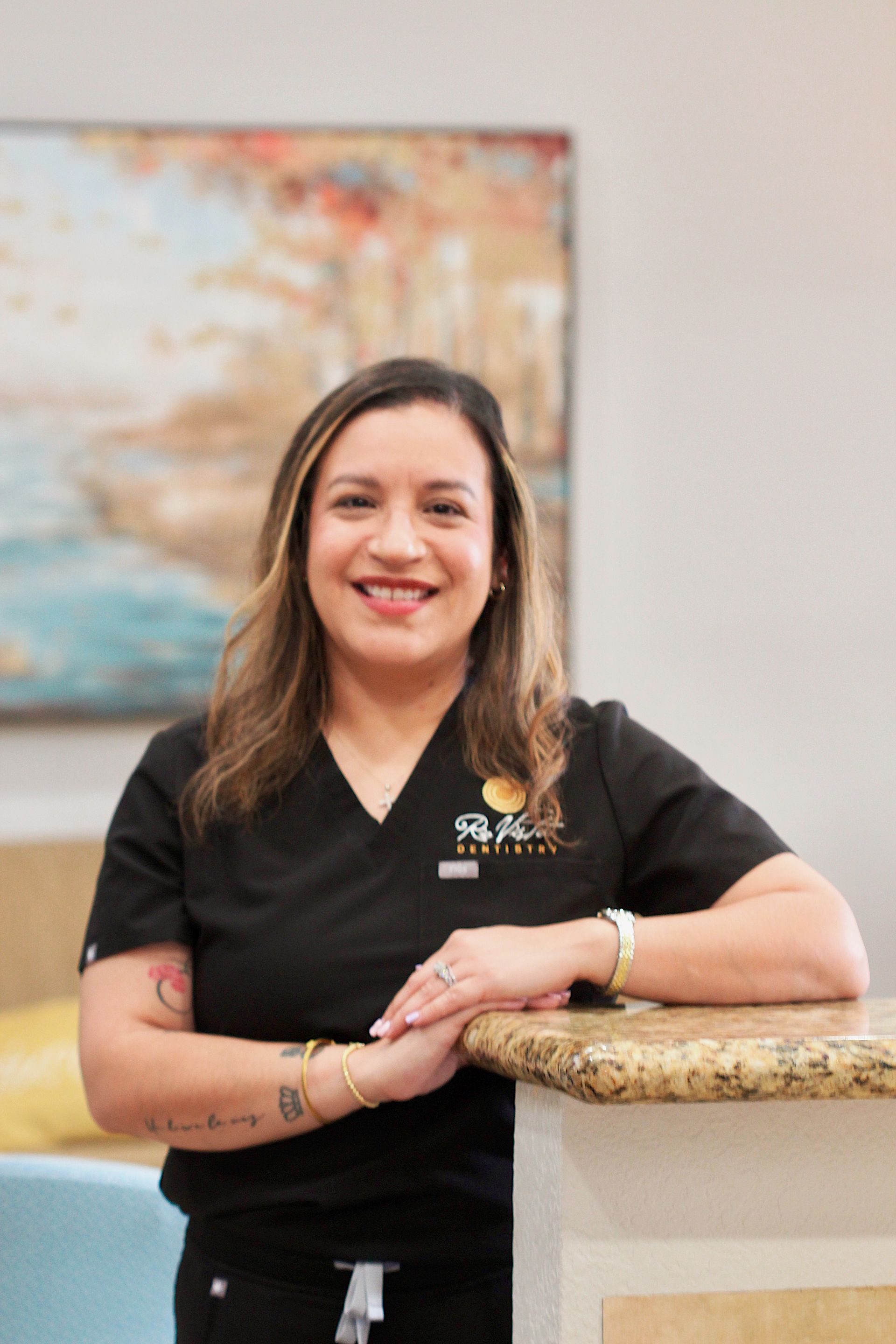 Smiling staff member in a black polo leaning on a counter in an office setting