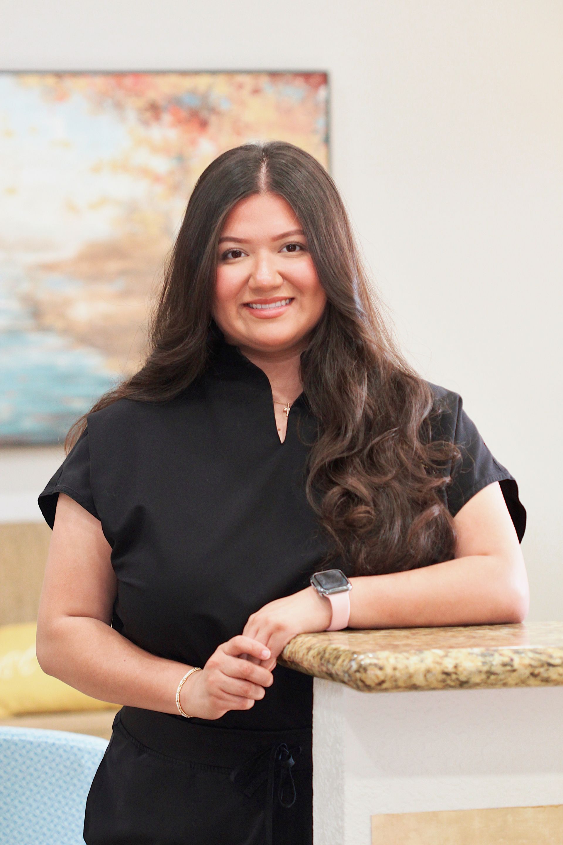 Woman in a black top leaning on a counter, smiling in a bright room with wall art.