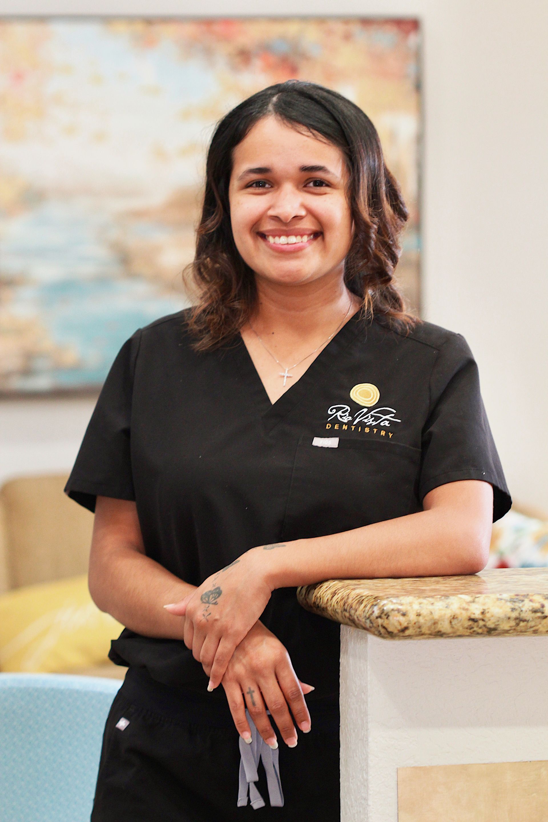 Smiling person in black scrubs standing by a countertop in a bright room
