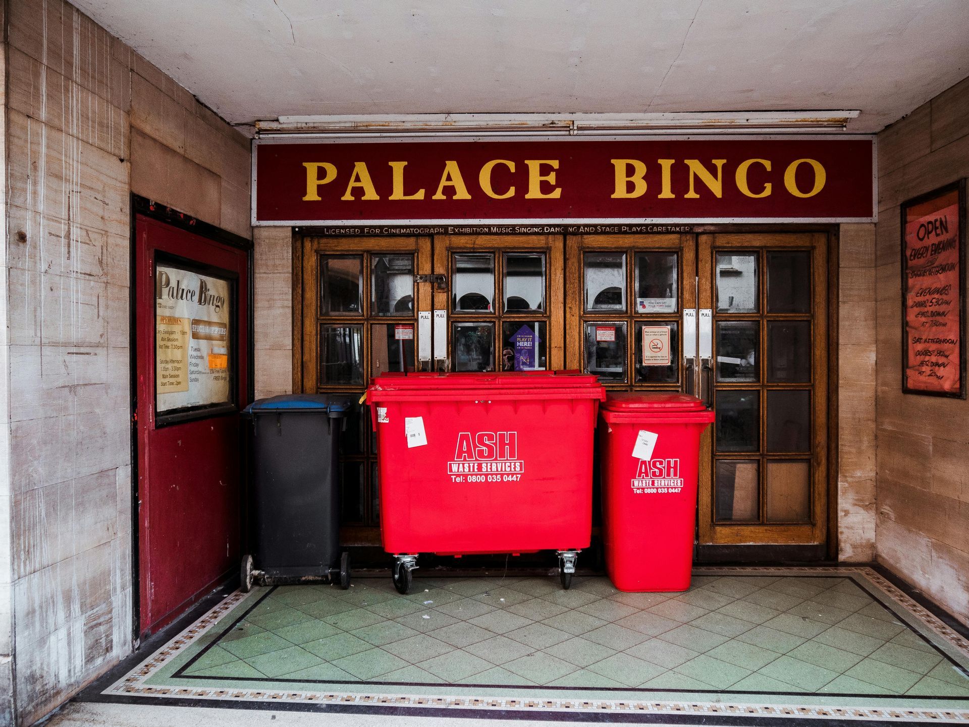 Palace Bingo entrance, red sign over doors, with three trash bins in front.