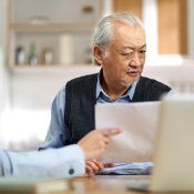 An elderly man is sitting at a table looking at a piece of paper.