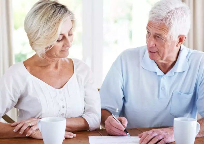 an elderly couple is sitting at a table signing a document .