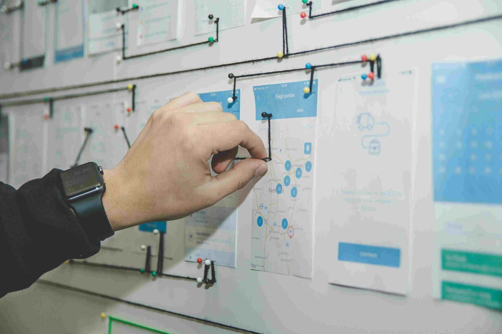 Hand connecting diagrams on a whiteboard with pushpins and lines, possibly for UX design or planning.