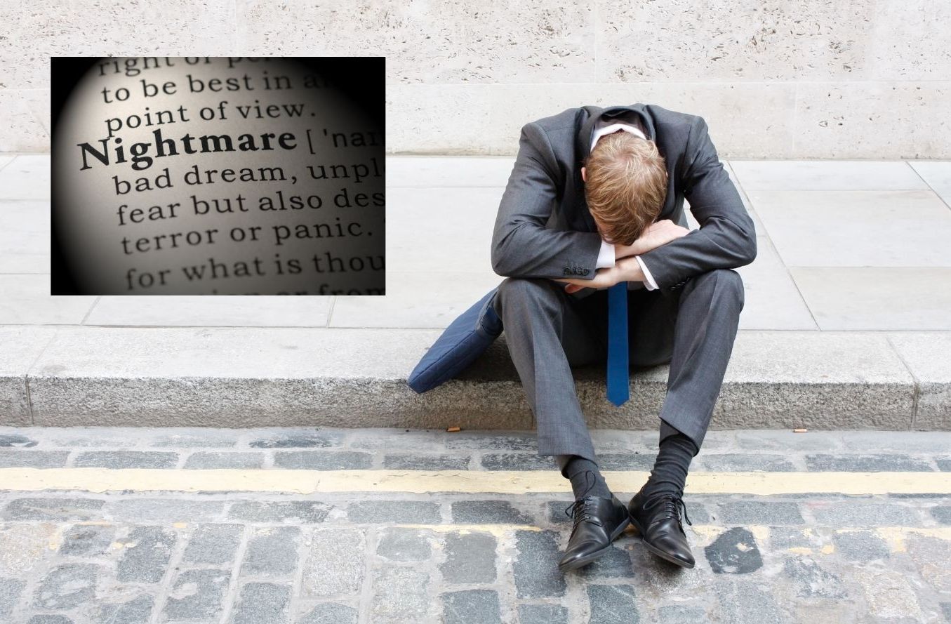A man in a suit sits on the sidewalk with his head down