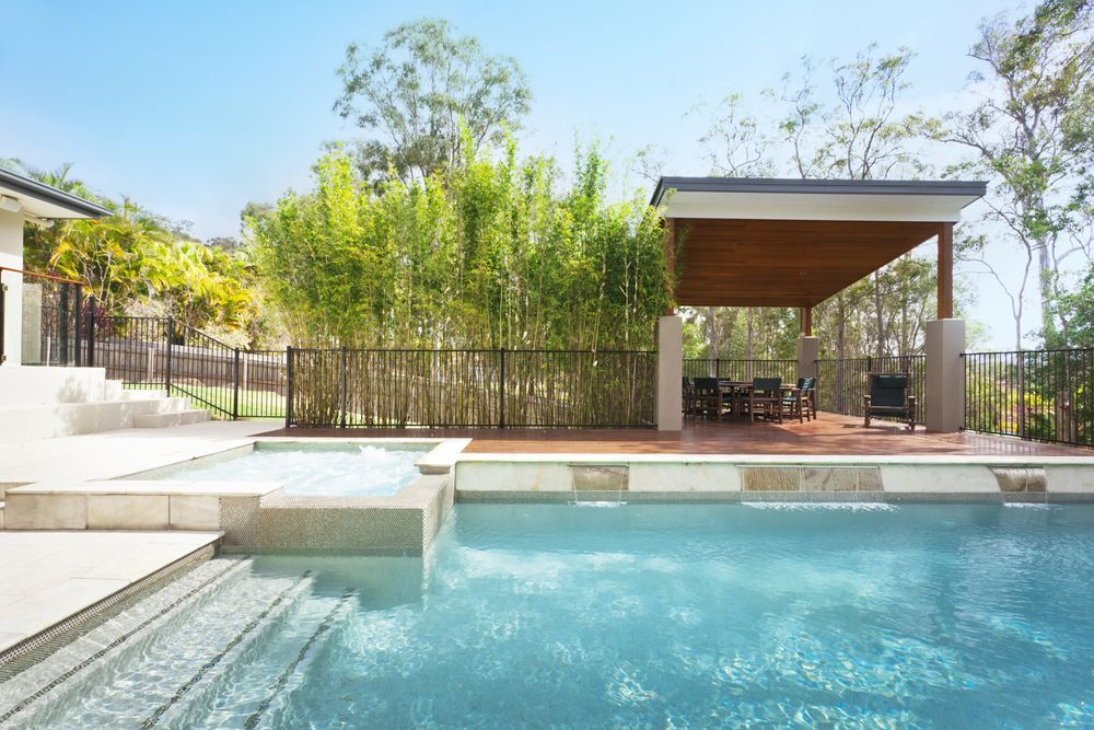 A swimming pool with a raised spa and a covered patio area surrounded by bamboo plants on a sunny day — Sand & Stone in Worongary, QLD