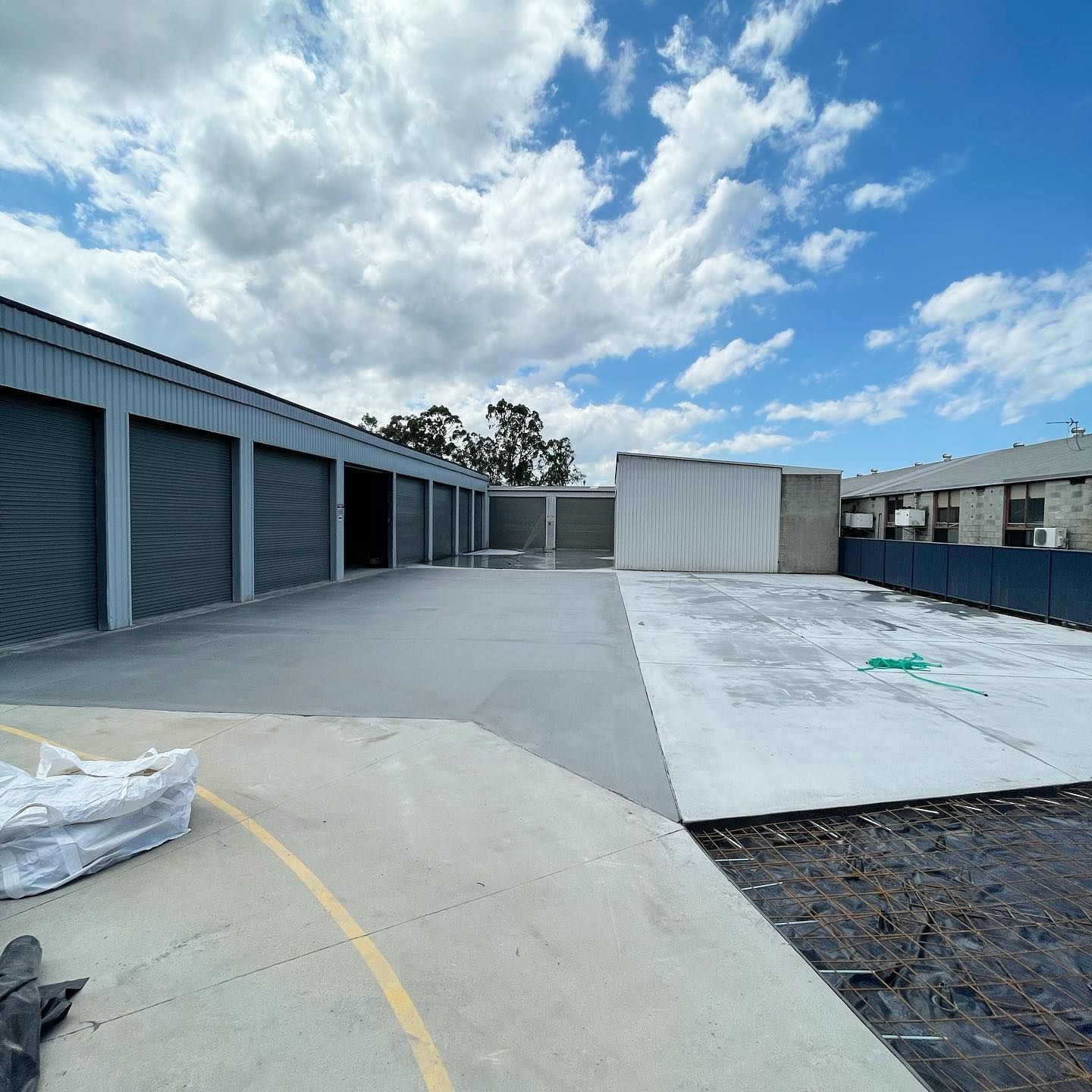 A Row of Industrial Storage Units With Grey Roller Doors Next to a Concrete Yard — Sand & Stone in Worongary, QLD
