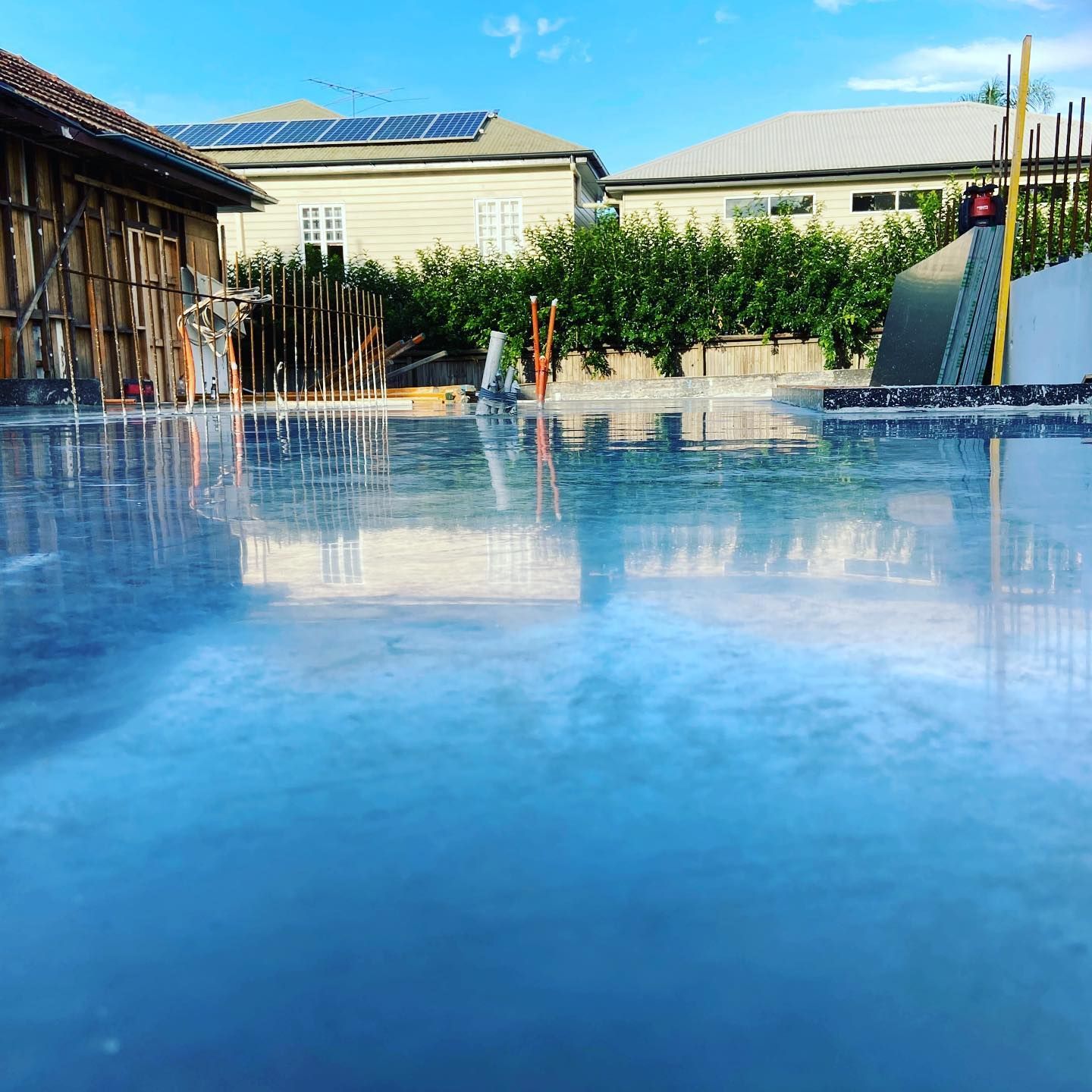 A reflective, polished blue concrete surface in a construction area with nearby houses and foliage under a sunny sky — Sand & Stone in Worongary, QLD