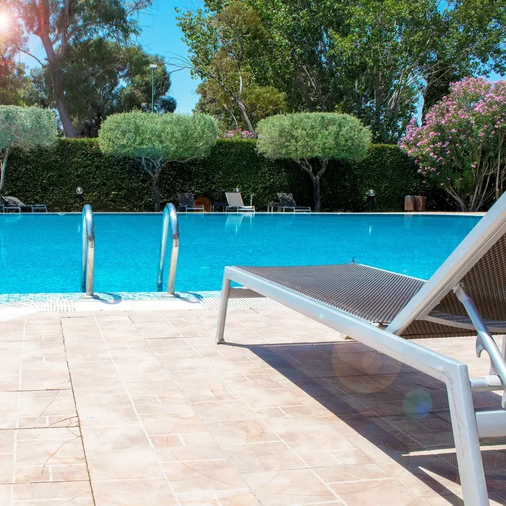 A sunny poolside scene with a lounge chair in the foreground, overlooking a bright blue swimming pool and manicured trees. — Sand & Stone in Tweed Heads, QLD