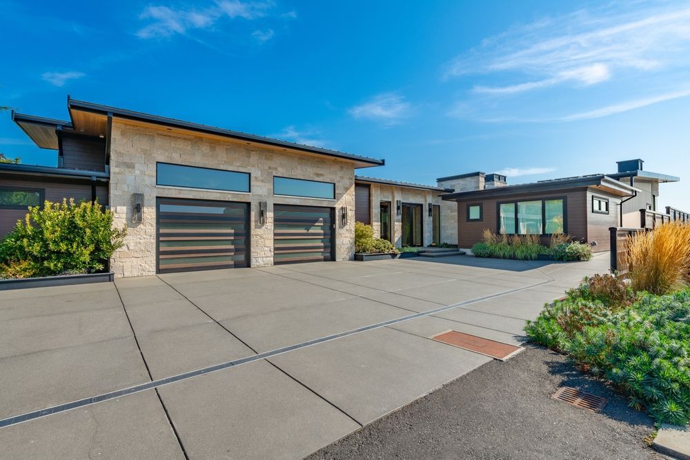 A modern, single-story home with a stone facade, flat roof, and a large concrete driveway under a clear blue sky — Sand & Stone in Worongary, QLD