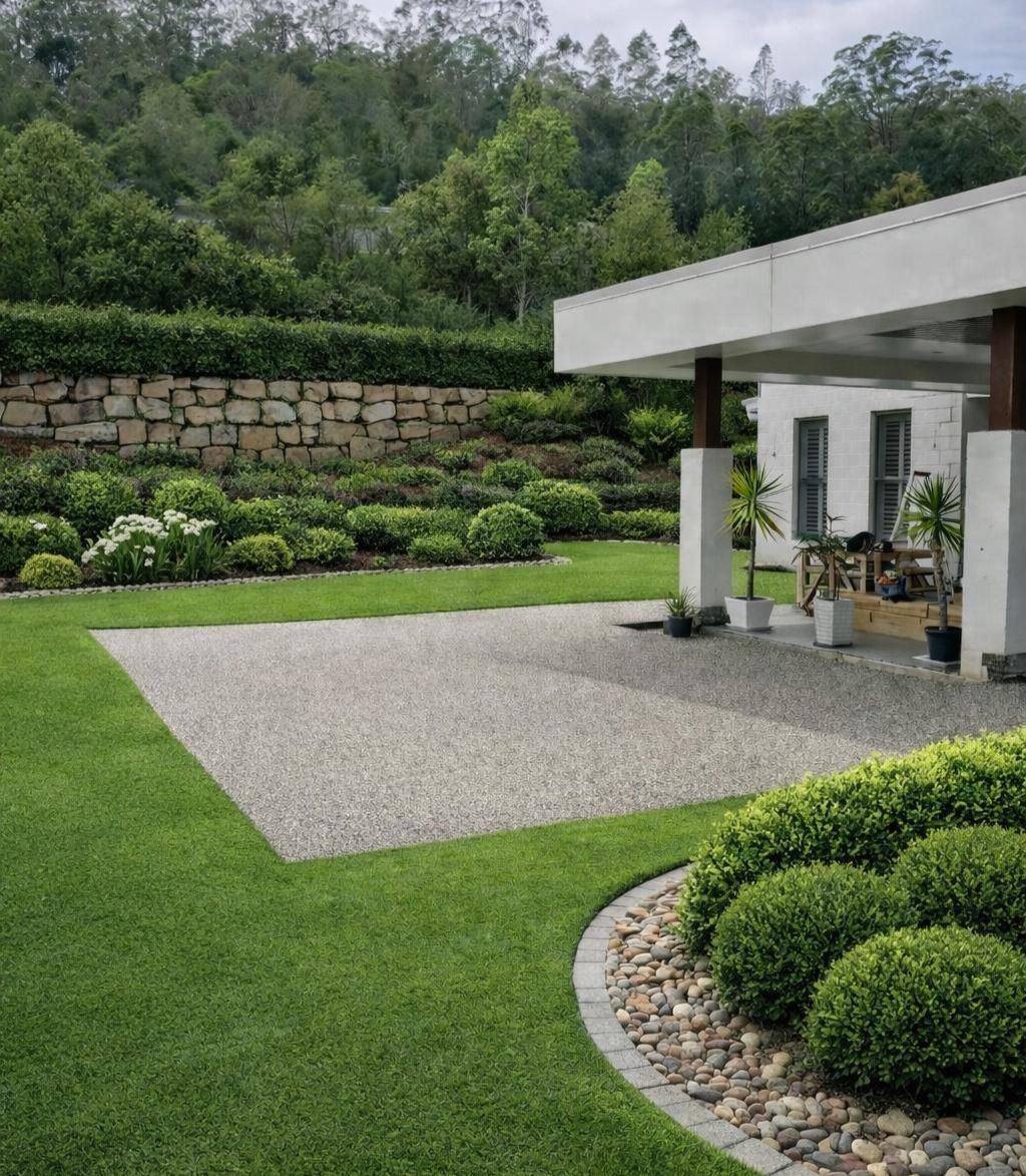 A landscaped yard with a gravel patio, mowed lawn, manicured shrubs, and a stone retaining wall near a modern home — Sand & Stone in Worongary, QLD
