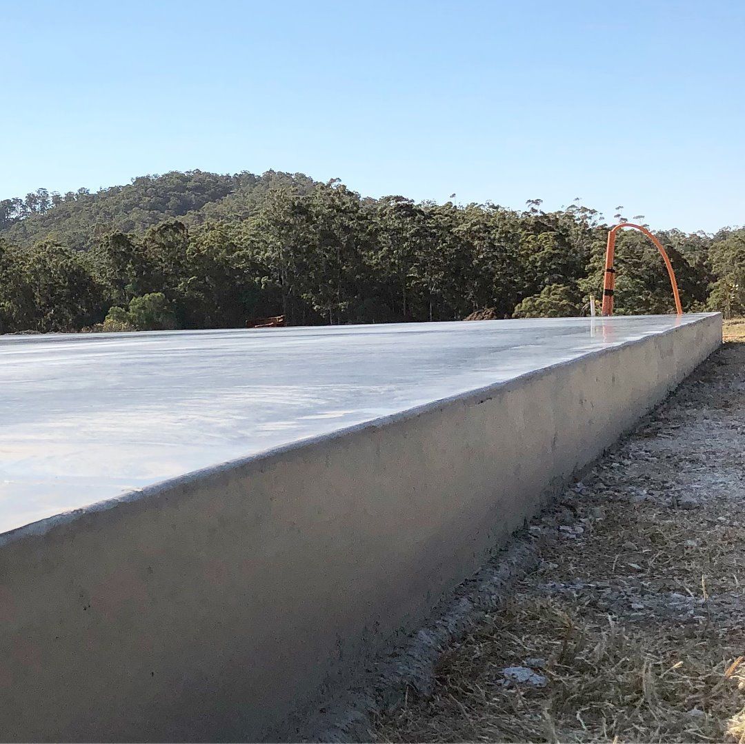 A newly poured, flat concrete foundation slab set in a field with trees in the background under a clear blue sky. — Sand & Stone in Worongary, QLD