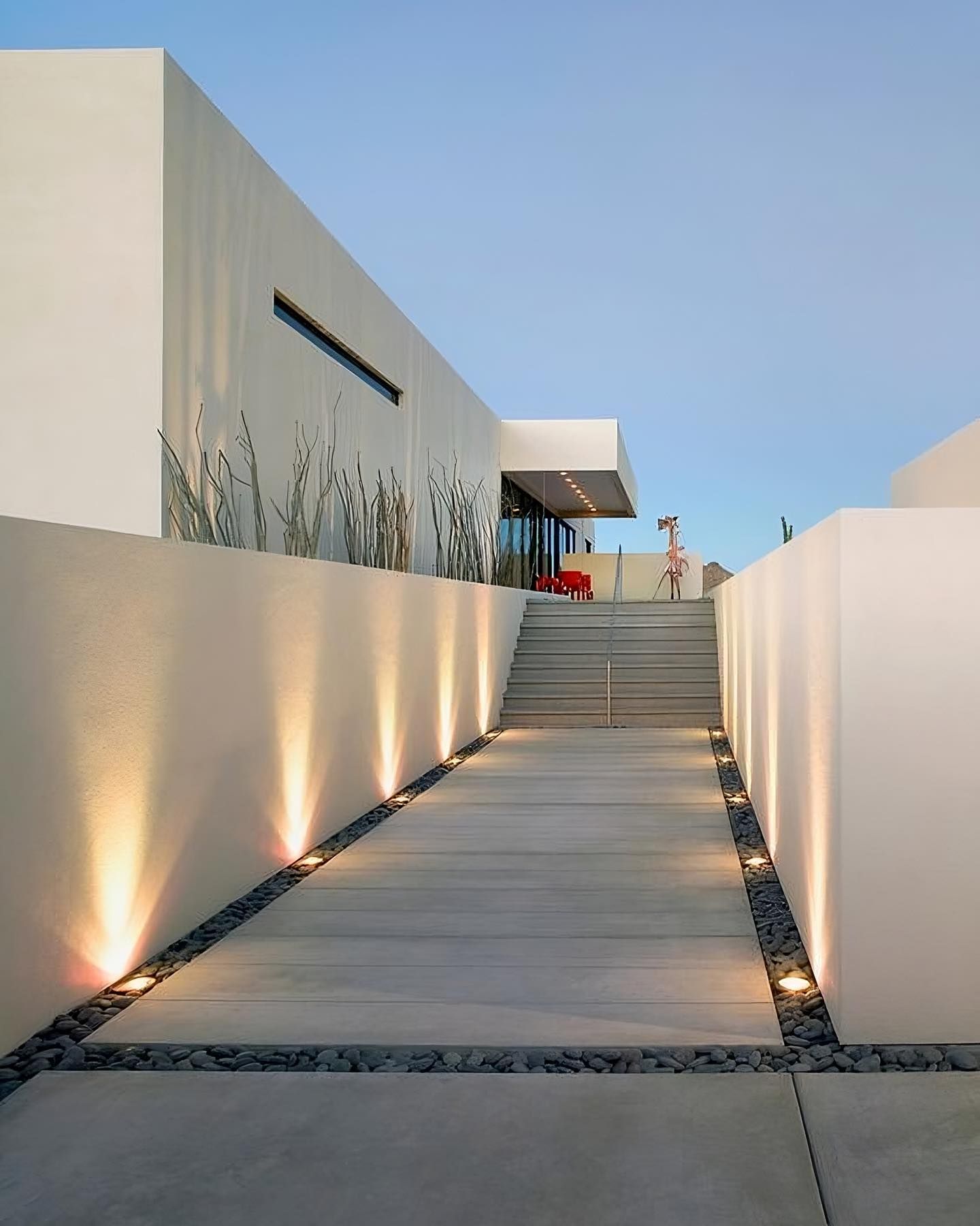 A modern white building entrance with a concrete walkway illuminated by ground lights, flanked by dark gravel borders. — Sand & Stone in Worongary, QLD
