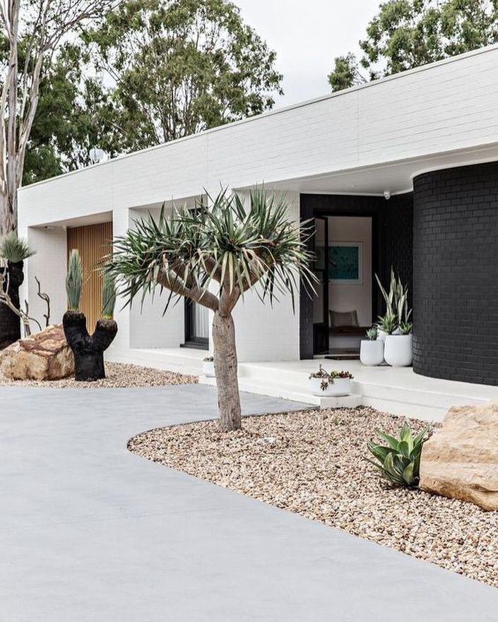 Modern home exterior with white and black brick walls, desert landscaping, gravel, large rocks, and a small palm tree. — Sand & Stone in Worongary, QLD