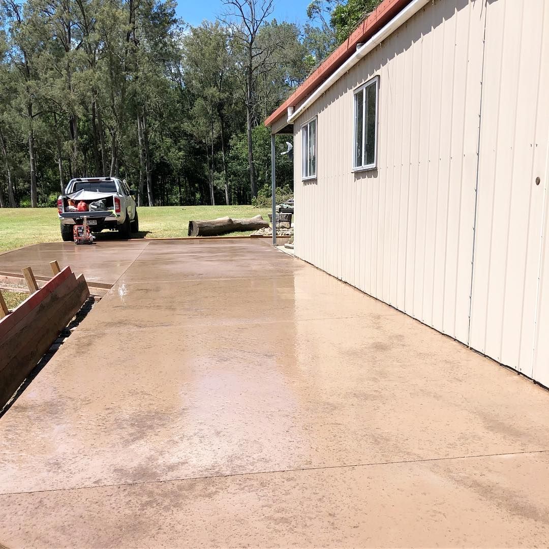 A Beige Metal Shed Stands Beside a Freshly Poured Concrete Driveway — Sand & Stone in Robina, QLD