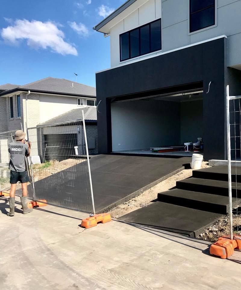 A Person Stands Near a New Dark Grey Concrete Driveway Ramp — Sand & Stone in Burleigh Heads, QLD