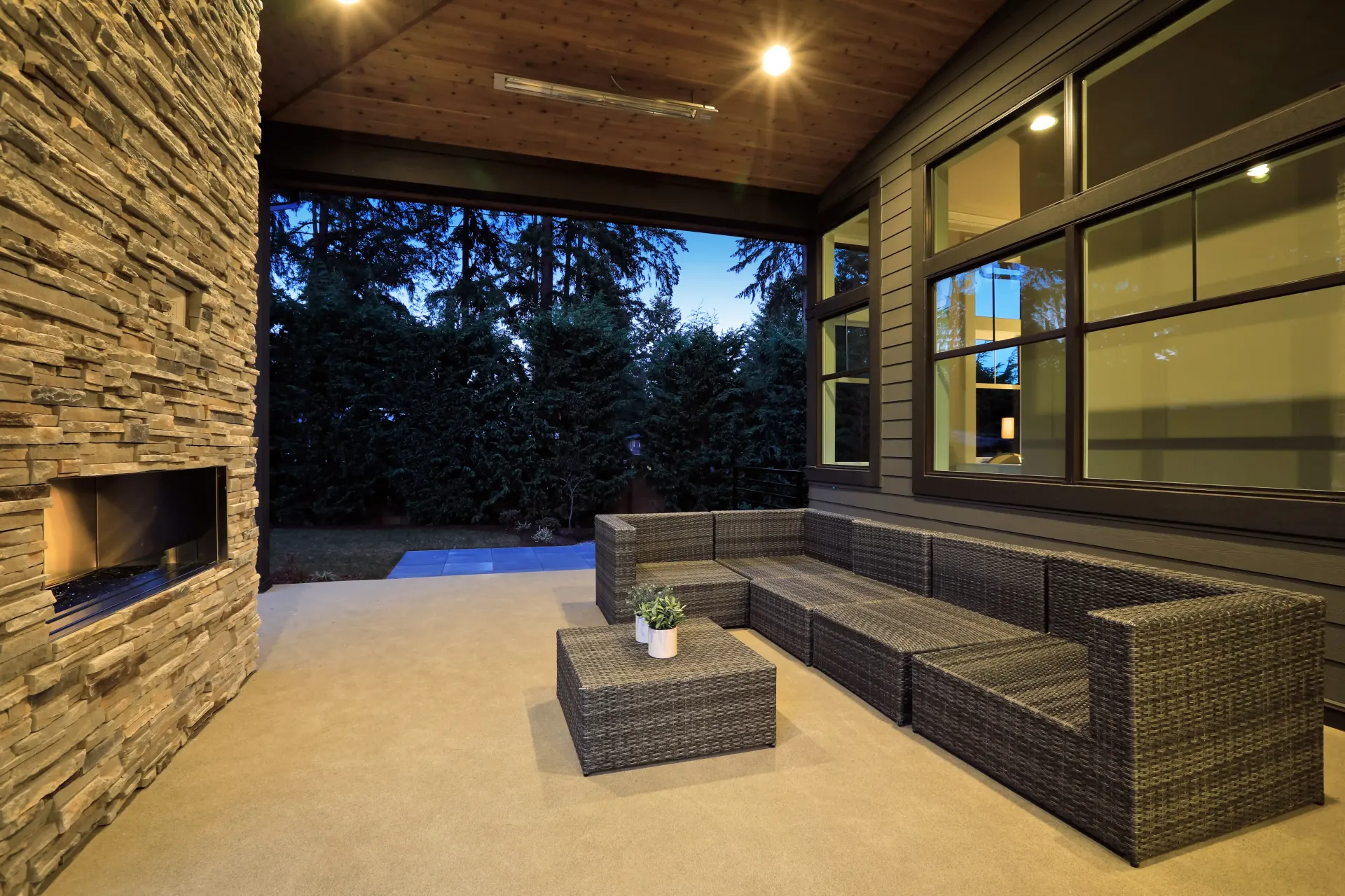 A covered patio featuring a stone fireplace, a large dark modular sofa with a matching coffee table, and wood ceiling — Sand & Stone in Worongary, QLD
