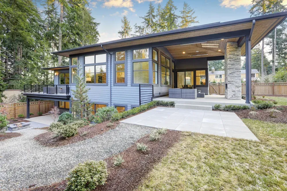A modern house with gray siding, a stone pillar, and a covered patio, set in a wooded backyard with a stone walkway — Sand & Stone in Worongary, QLD