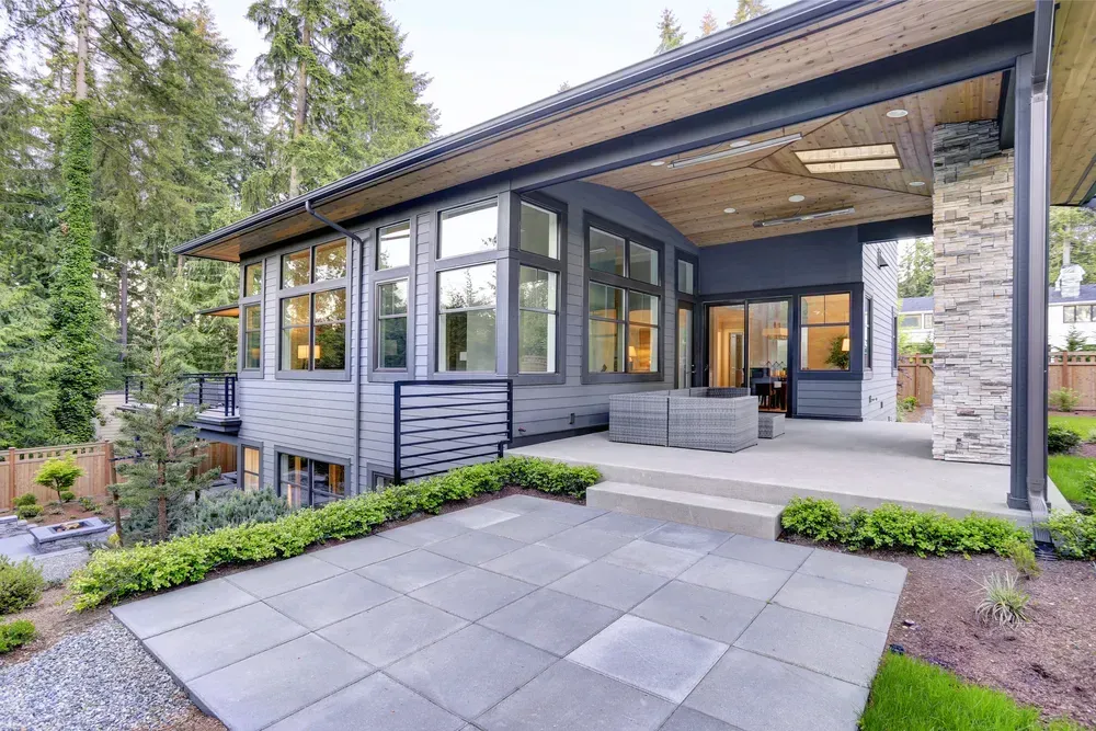 Modern house exterior with a paved patio, stone pillar, and covered deck area surrounded by trees. — Sand & Stone in Worongary, QLD