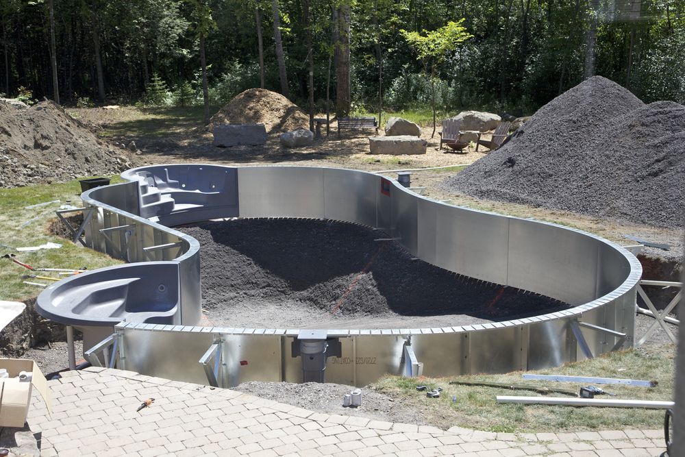 An in-ground swimming pool under construction with metal walls, gray steps, and a dark gravel base in a backyard — Sand & Stone in Worongary, QLD