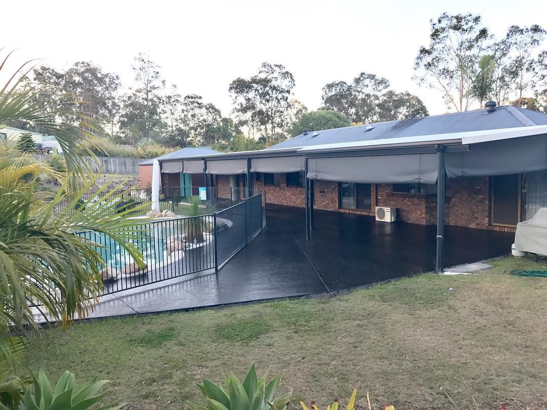 A backyard featuring a brick house with a covered patio, black concrete flooring, and a fenced swimming pool. — Sand & Stone in Worongary, QLD