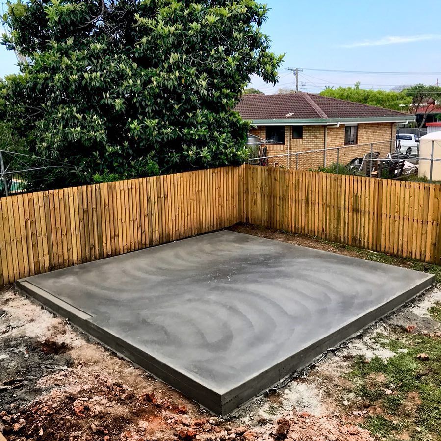 A freshly poured rectangular concrete pad sits in a backyard, enclosed by a bamboo fence with a house in the background. — Sand & Stone in Tweed Heads, QLD