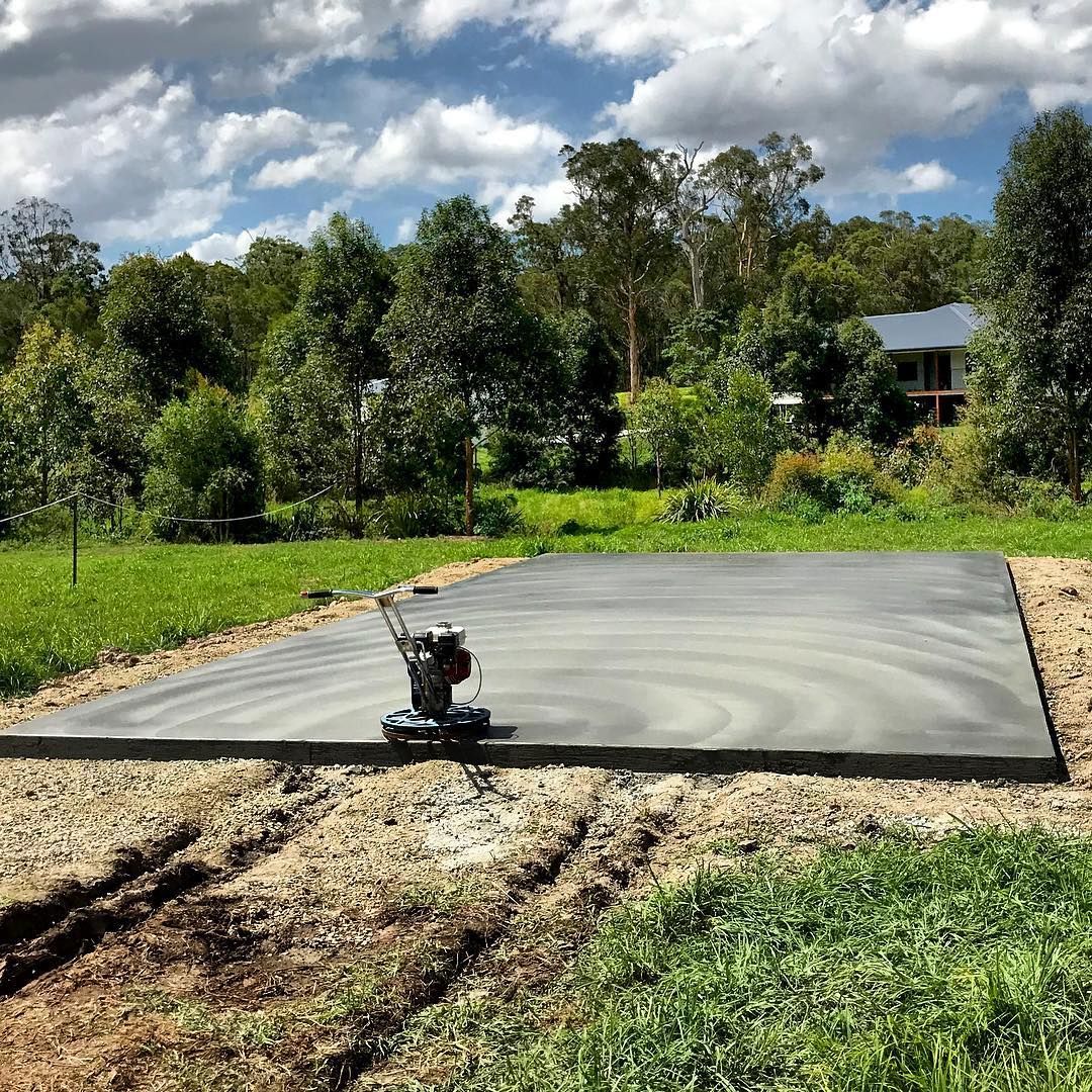 A newly poured, flat concrete slab sits in a grassy yard, with a power trowel machine left on its surface — Sand & Stone in Worongary, QLD