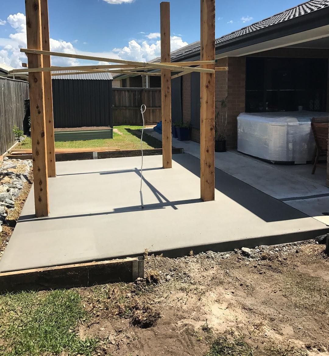 A newly poured concrete slab in a backyard with four tall wooden posts standing on it under a clear sky. — Sand & Stone in Worongary, QLD