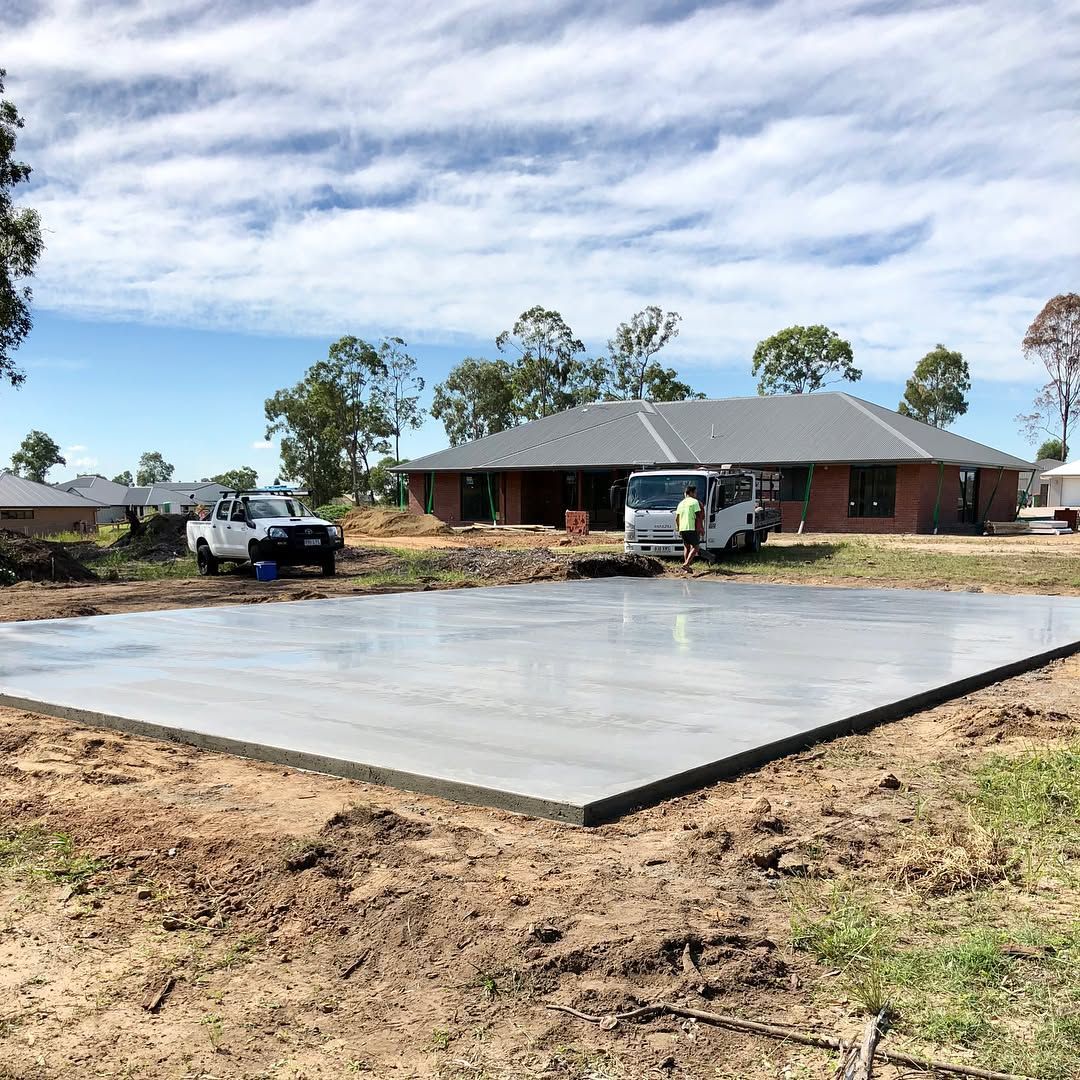 A freshly poured concrete slab in a residential yard with a house, truck, and van in the background under a blue sky — Sand & Stone in Worongary, QLD