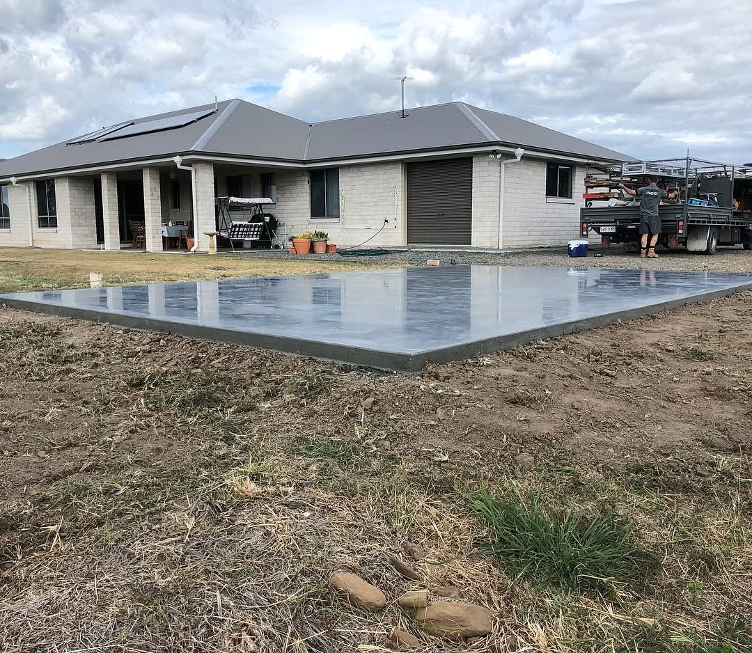 A freshly poured concrete slab sits in a yard in front of a modern, light-coloured single-story house. — Sand & Stone in Worongary, QLD