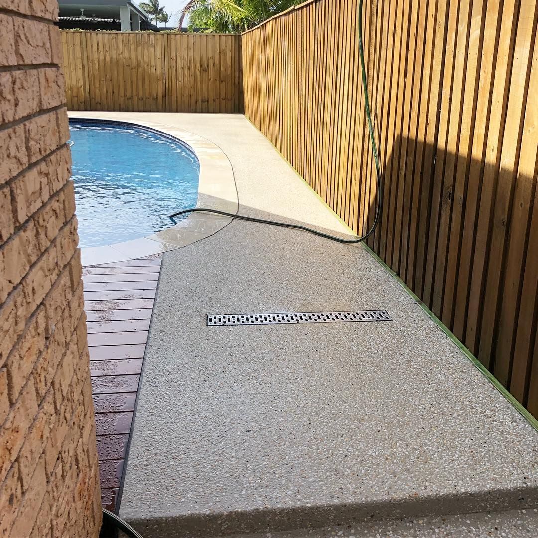 A poolside concrete path with a linear drainage grate, positioned between a brick wall and a wooden fence. — Sand & Stone in Worongary, QLD