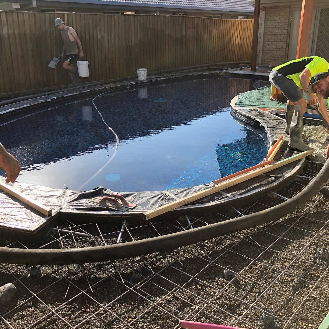 Workers pour concrete around a curved swimming pool in a backyard renovation project. — Sand & Stone in Worongary, QLD