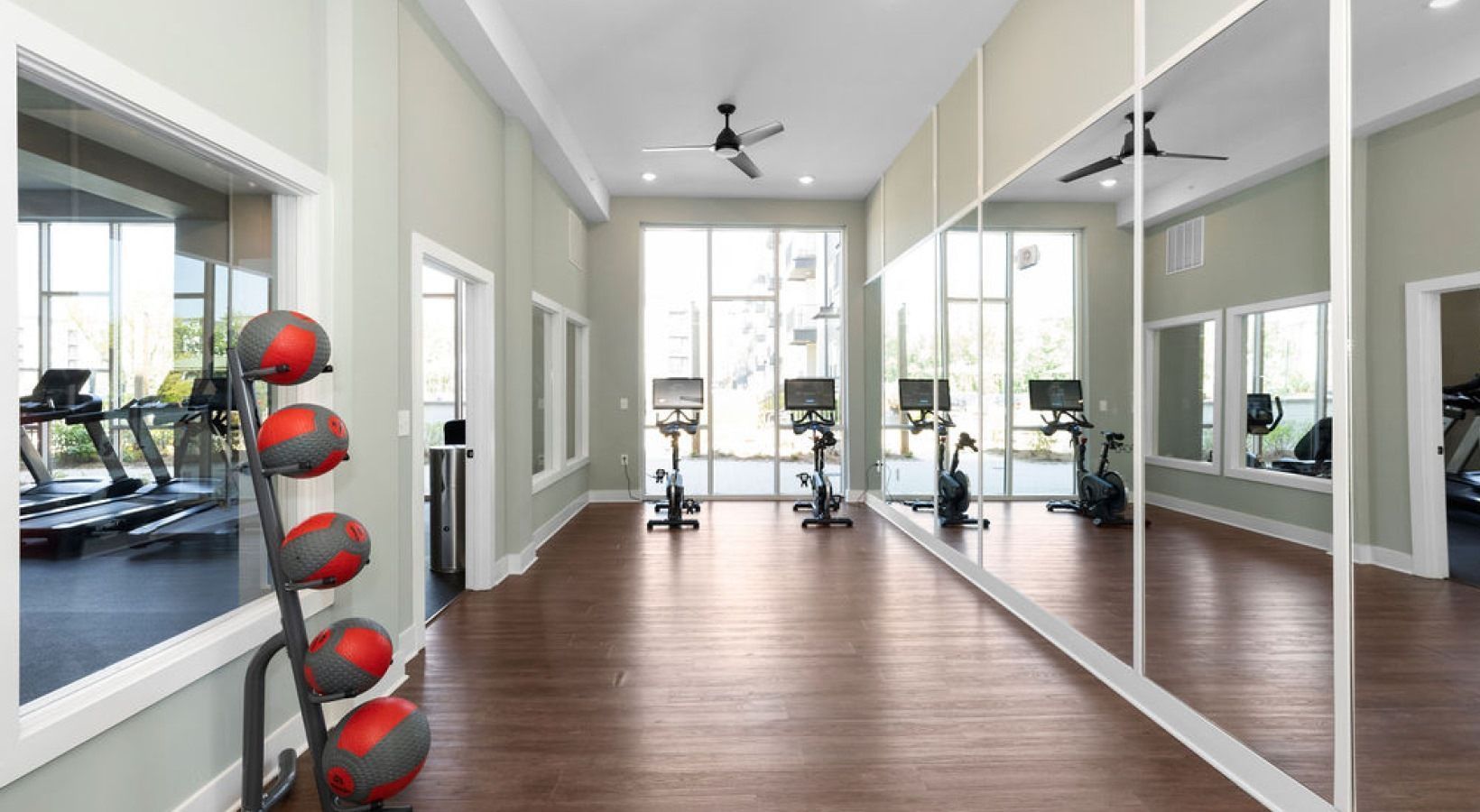 Gym with treadmills, exercise bikes, and medicine balls, large windows, and mirrors. We invite you to visit 1001 Tyvola and take a tour of our apartments with a fitness center in Mecklenburg County.
