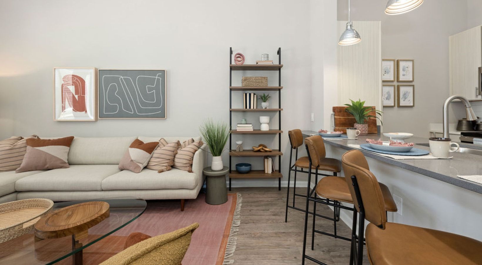 Living room with a sofa, bookshelf, kitchen island with barstools, and decor. We invite you to visit 1001 Tyvola and take a tour of our rentals near Metrolina Regional Scholars Academy in North Carolina.