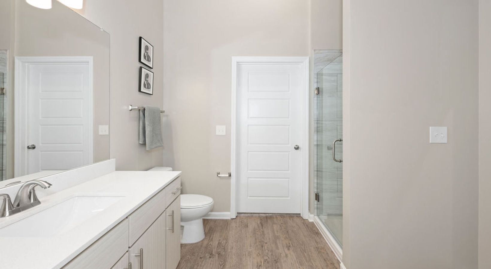Bathroom with white cabinets, toilet, shower, and gray walls with wood-look flooring. We invite you to visit 1001 Tyvola and take a tour of our apartments near Renaissance Park in Mecklenburg County.