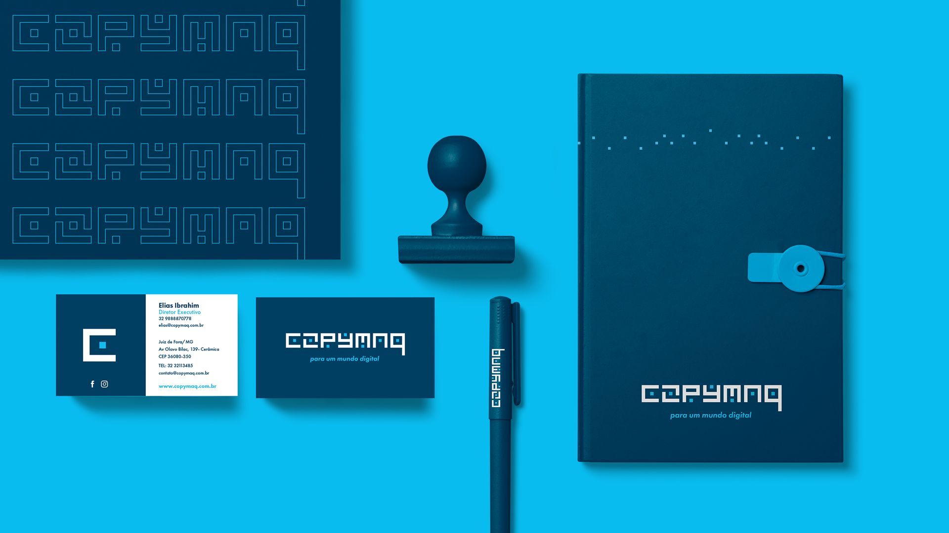 Conjunto de identidade visual corporativa com artigos de papelaria, caderno, caneta e carimbo em tons de azul escuro sobre um fundo azul claro.