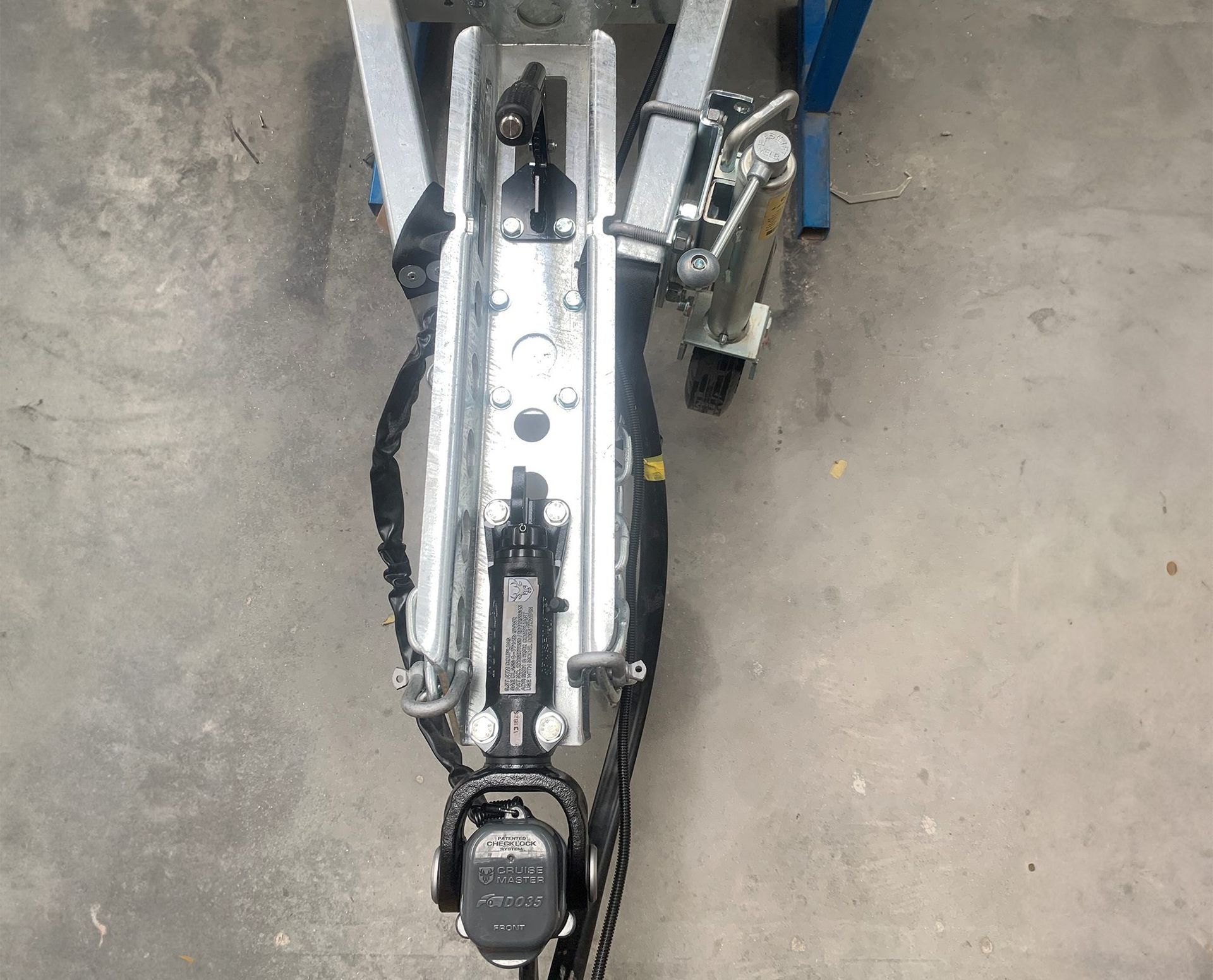 A high-angle view of a galvanized steel trailer tongue hitch assembly with a black coupling and safety chains.