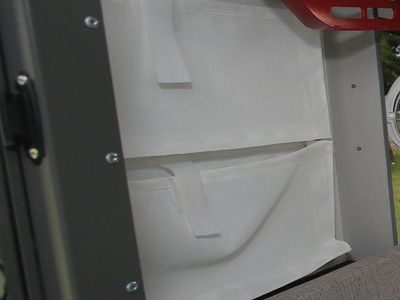 A close-up of white storage pouches with velcro straps attached to the interior wall of a gray metal transport case.