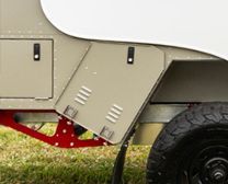 Close-up of a tan metal storage compartment with vents on a trailer, featuring a red chassis and a black tire.