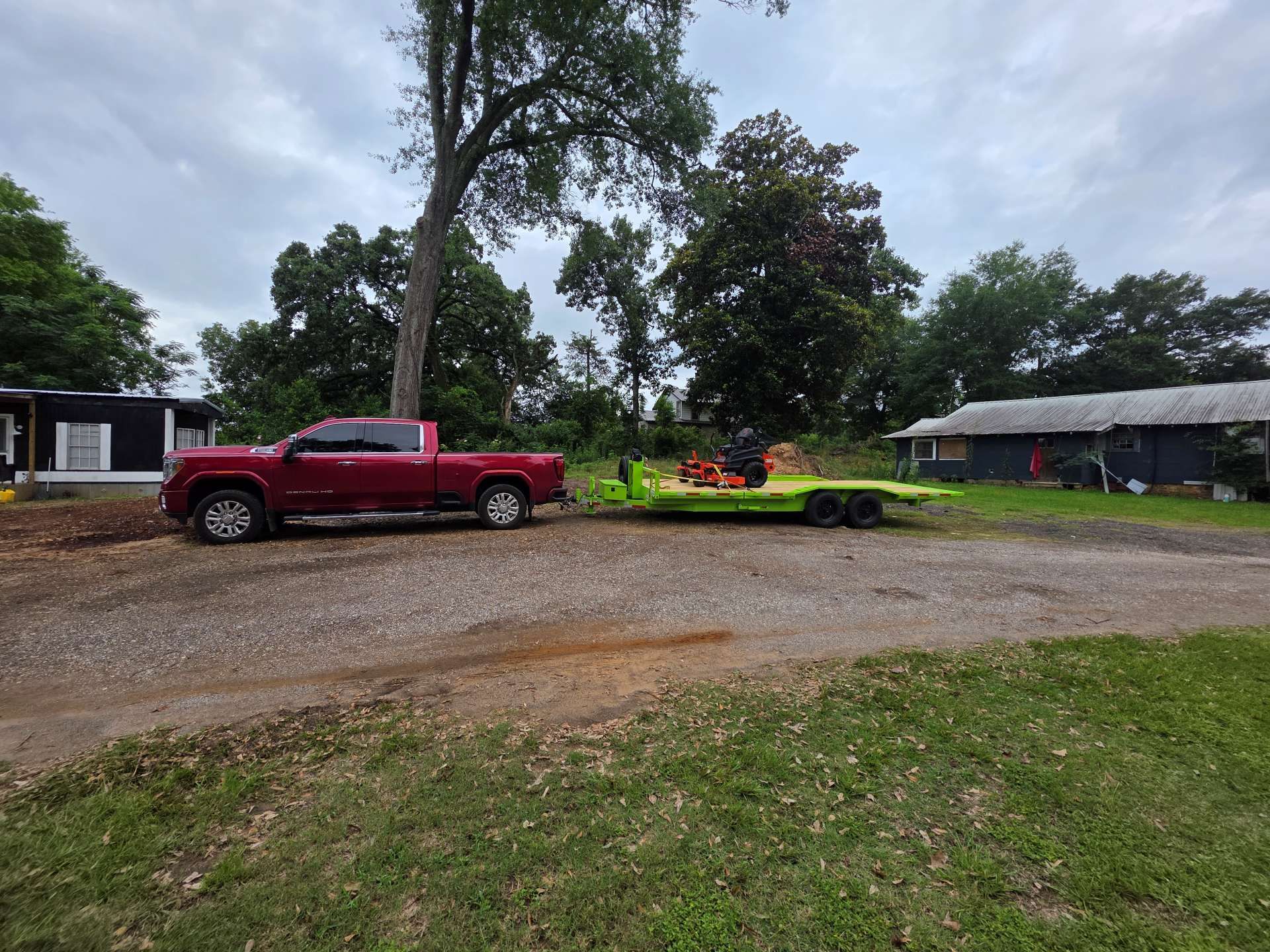 Red pickup truck parked by a gravel driveway with a low trailer and trees in the background