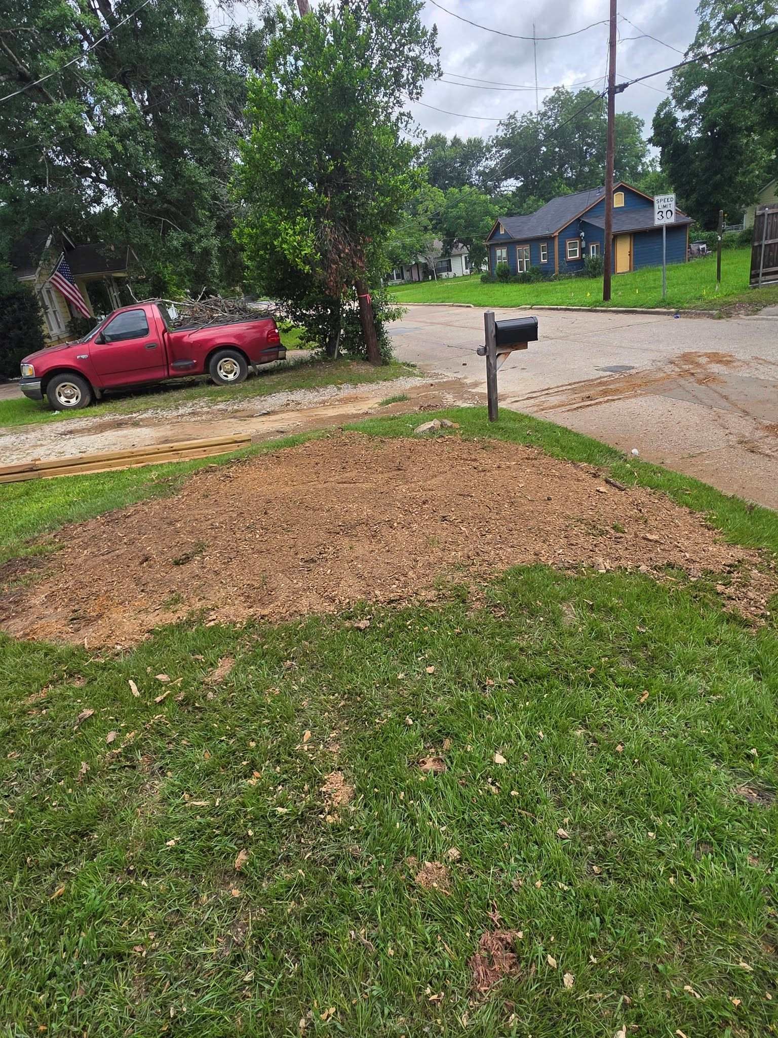 Gravel mound in a yard by a mailbox, with a red pickup truck and trees in the background.