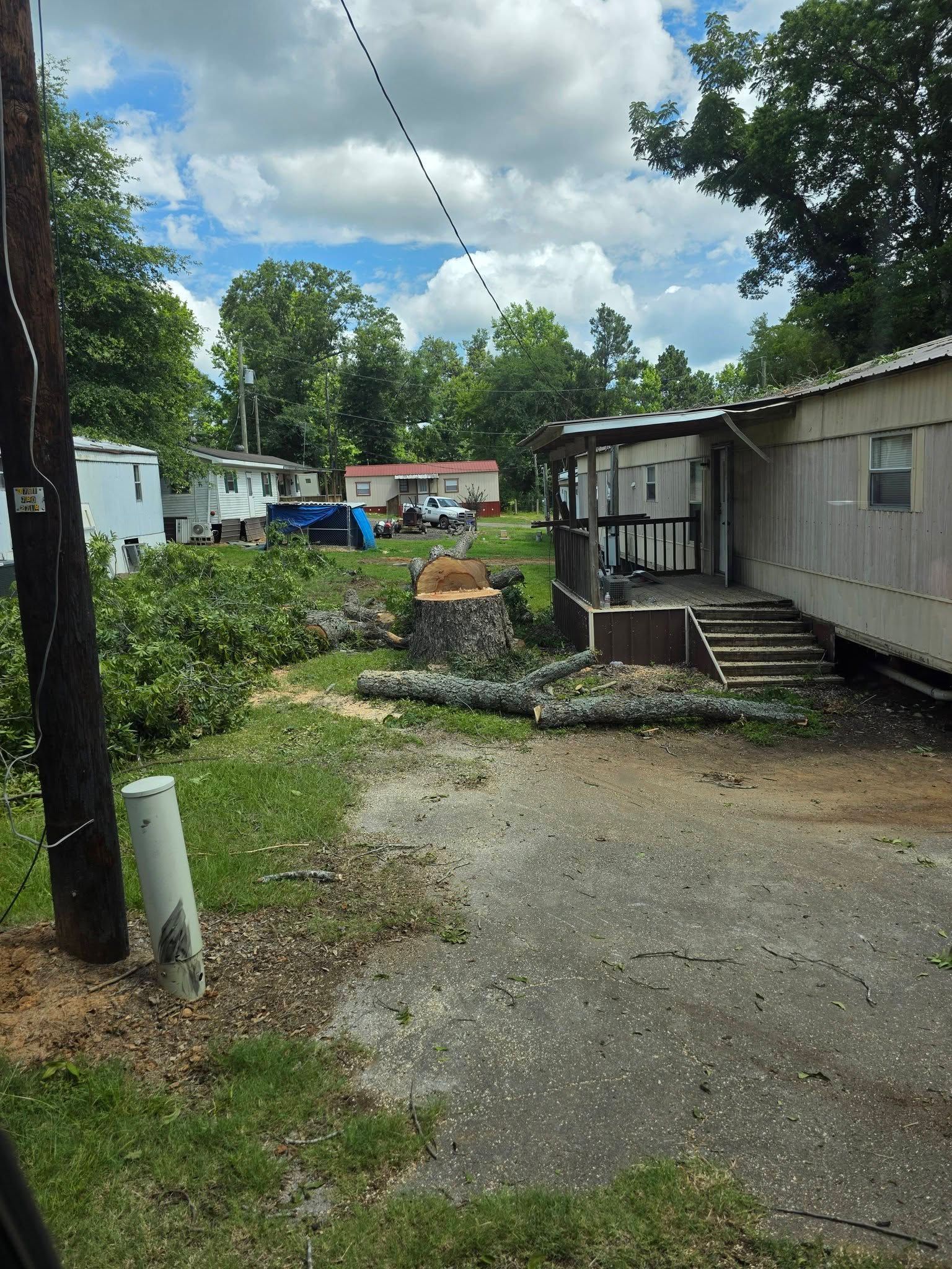 Mobile home lot with gravel driveway, trees, and scattered debris after storm damage