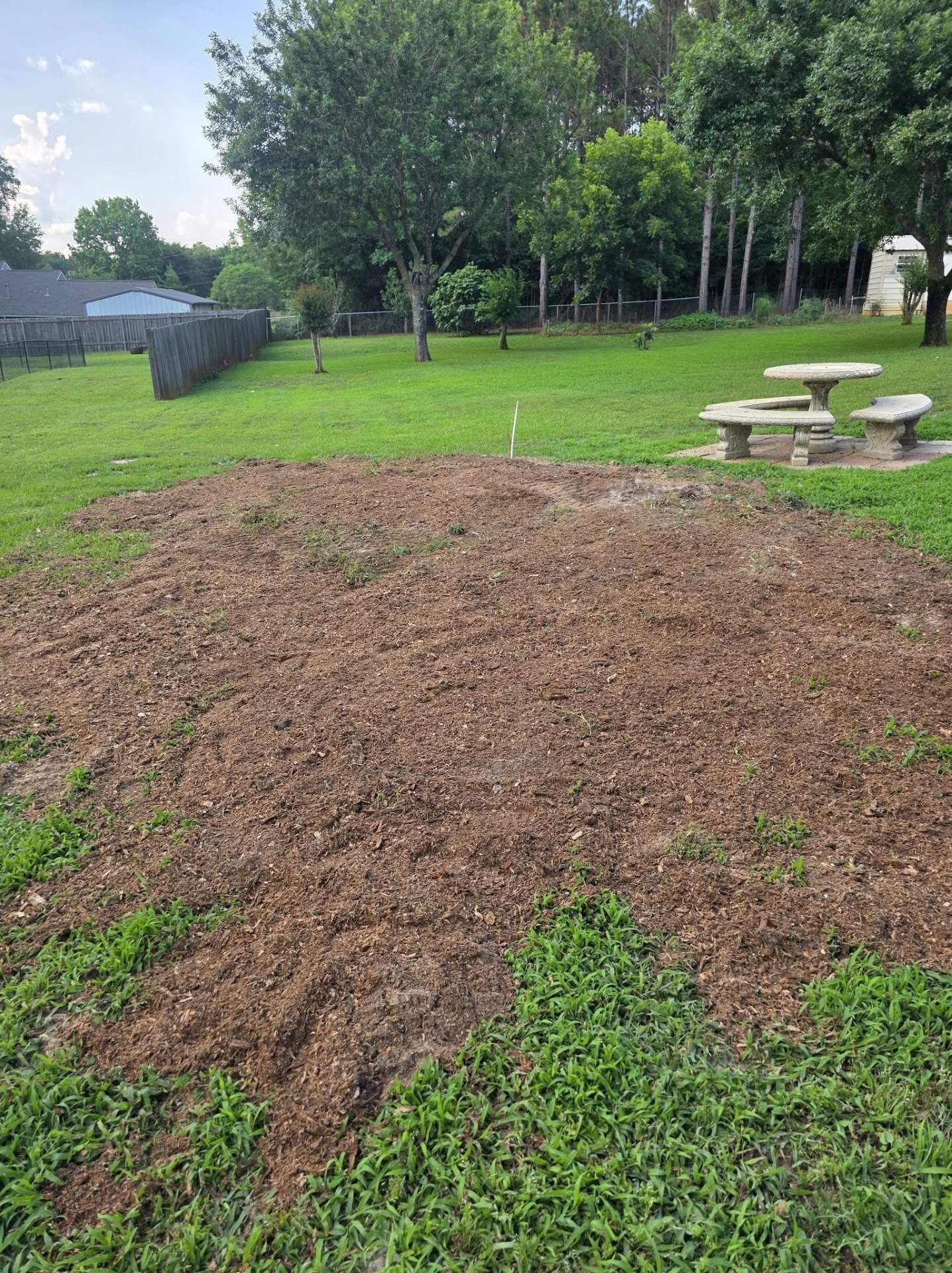 Large mound of brown dirt on a grassy park lawn near picnic tables and trees