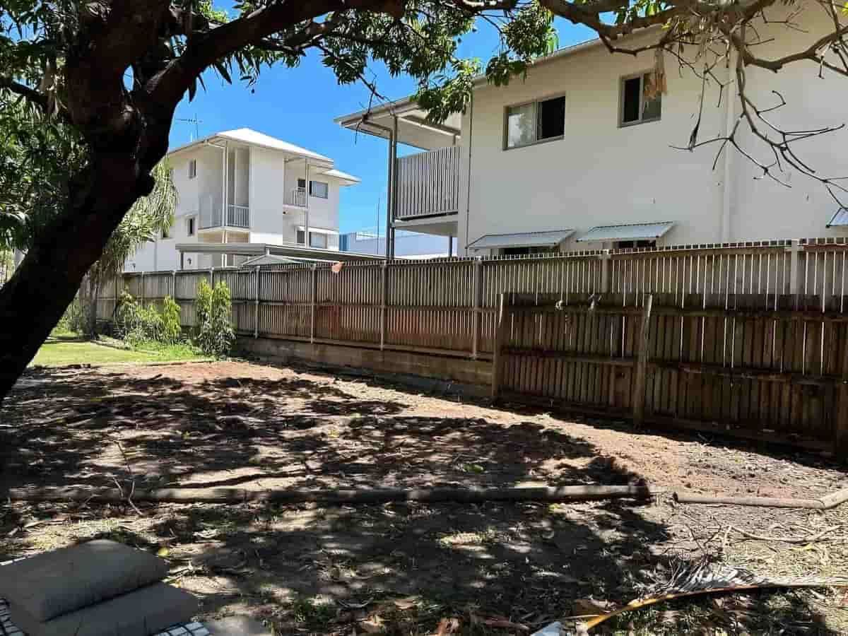 A Backyard With A Wooden Fence And A White House In The Background — Limburg Lawn & Property Maintenance In Hyde Park, QLD