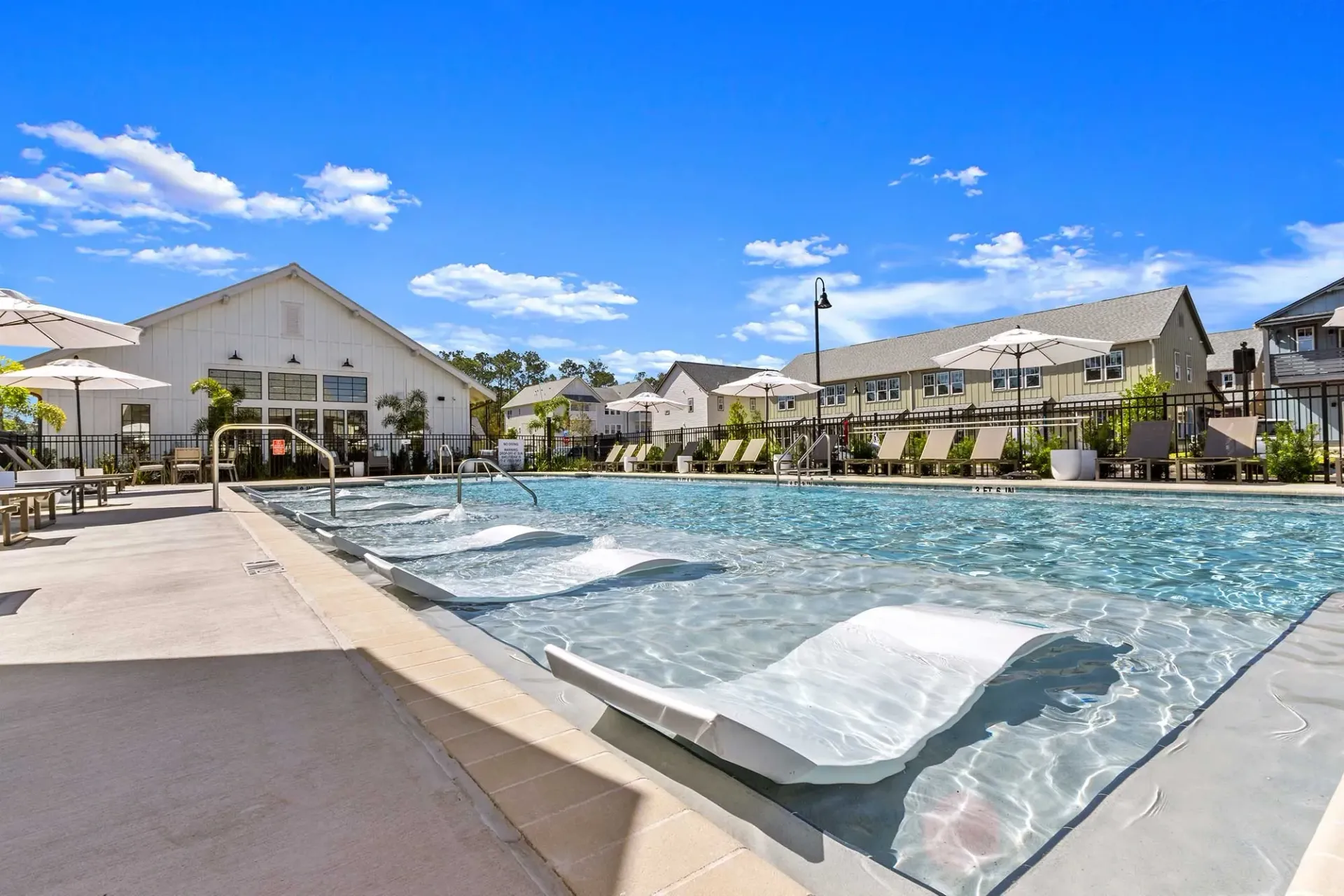 Modern apartment complex with a swimming pool and lounge chairs under a sunny blue sky