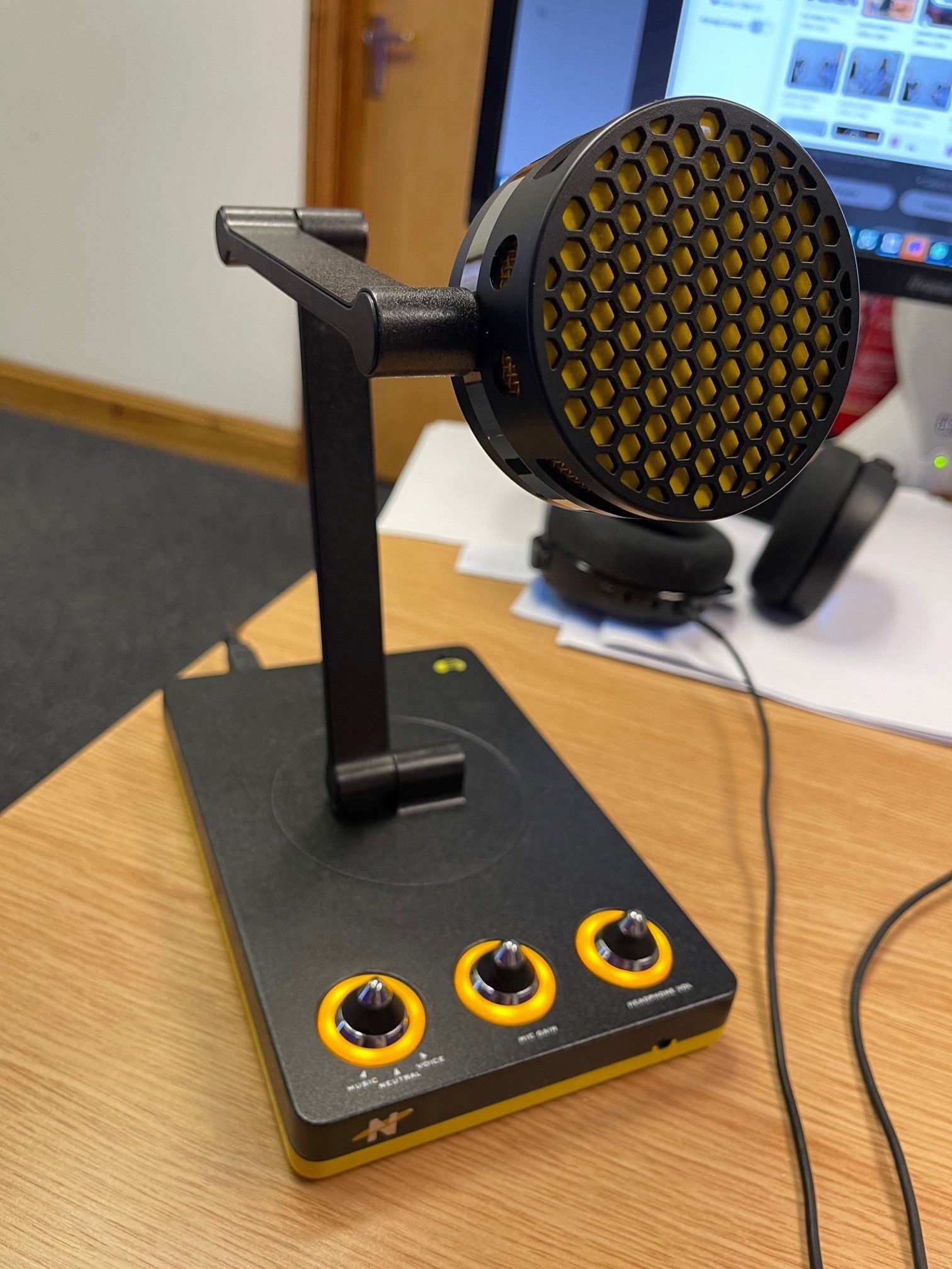 A microphone is sitting on a wooden table next to a computer monitor